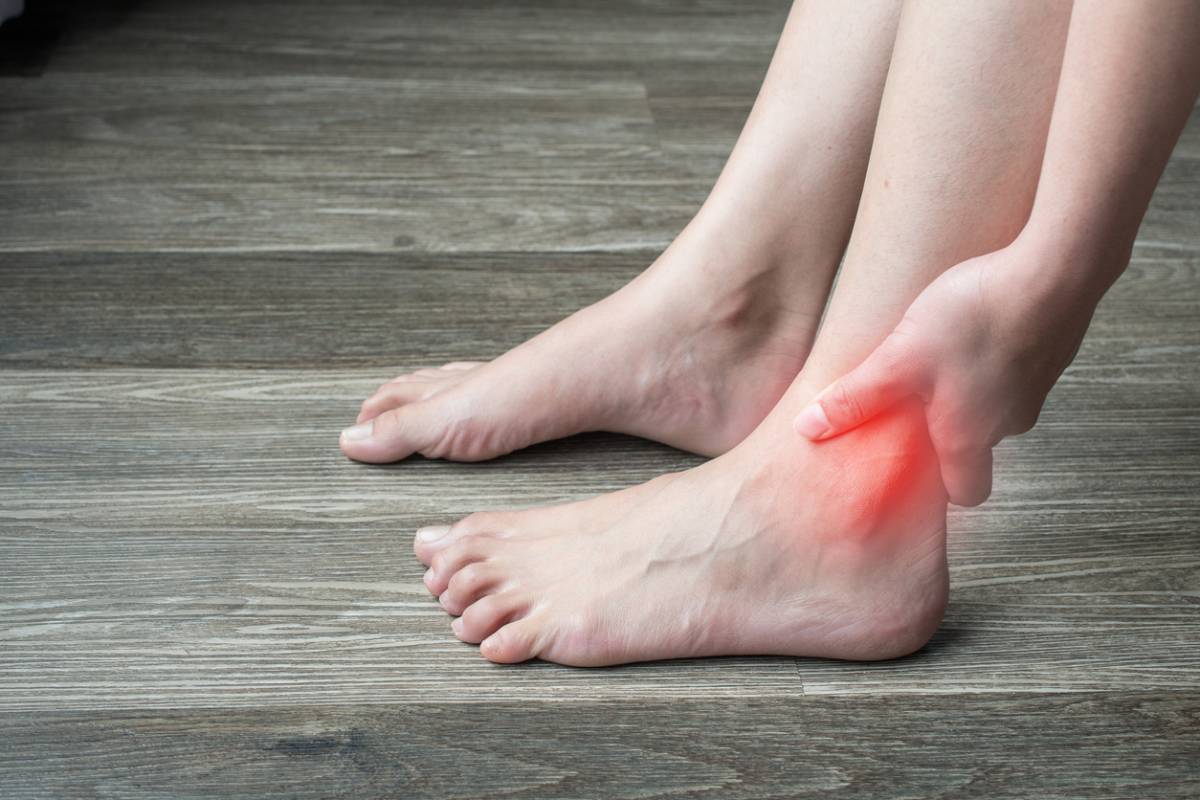 Close-up of woman hands holding and touching her ankle, suffering from ankle pain.
